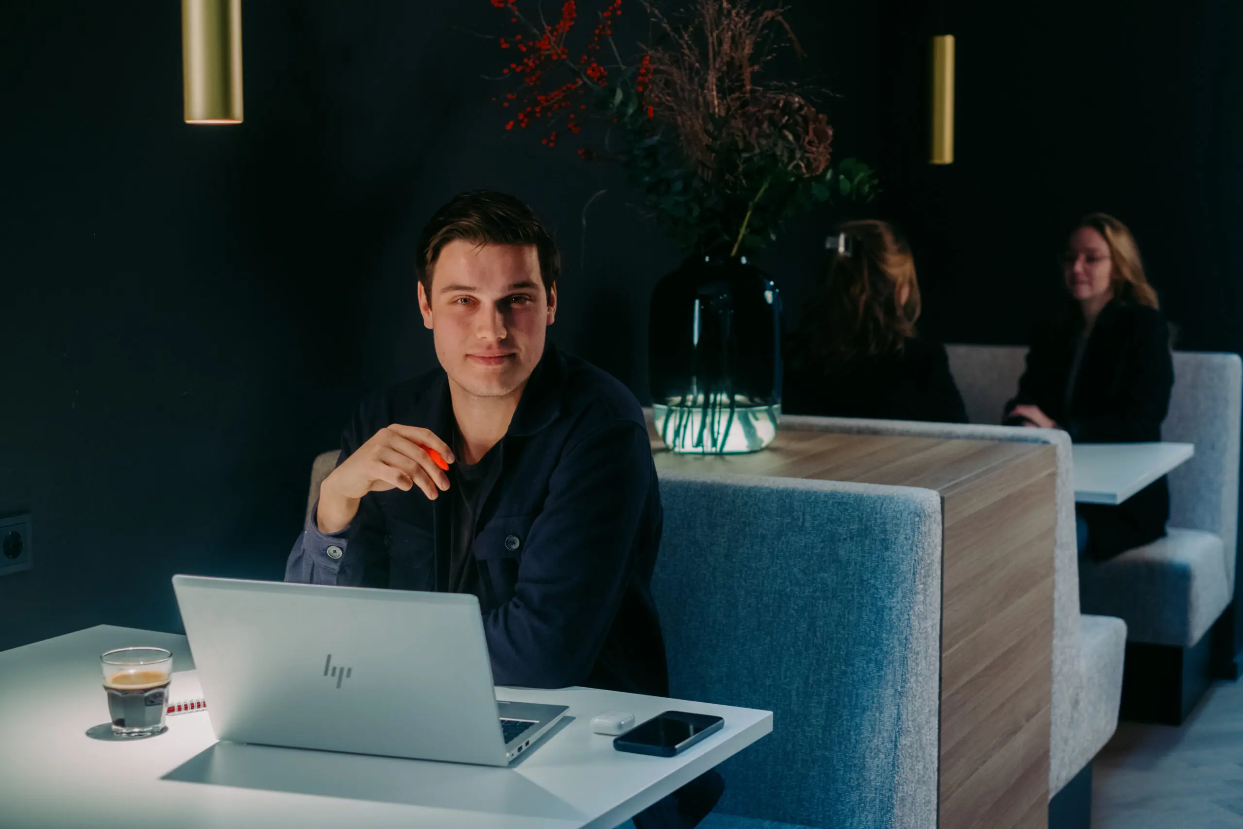 Een man werkt op een laptop in een modern café met een donkere inrichting.
