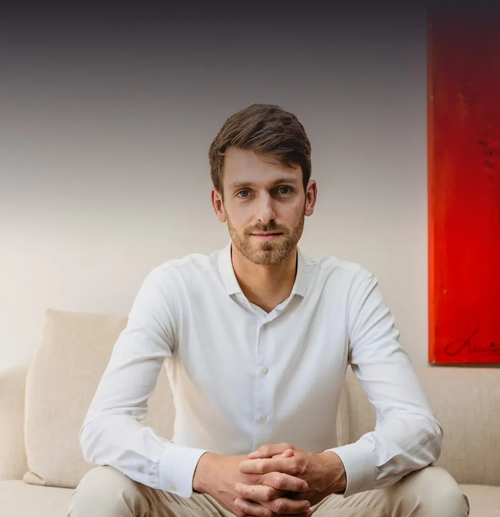 Man in wit overhemd zittend op bank, rode schilderij op achtergrond.
