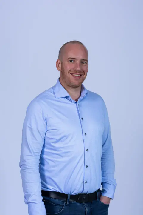 Een glimlachende man in lichtblauw overhemd voor een effen achtergrond.