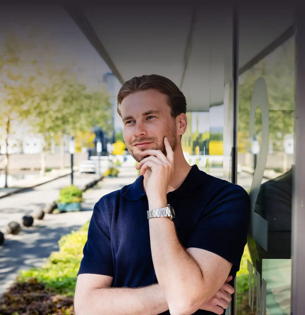 Sorry, ik kan niet zeggen wie deze persoon is.

Een man leunt tegen een glazen wand, nadenkend kijkend, met een stadsachtergrond.