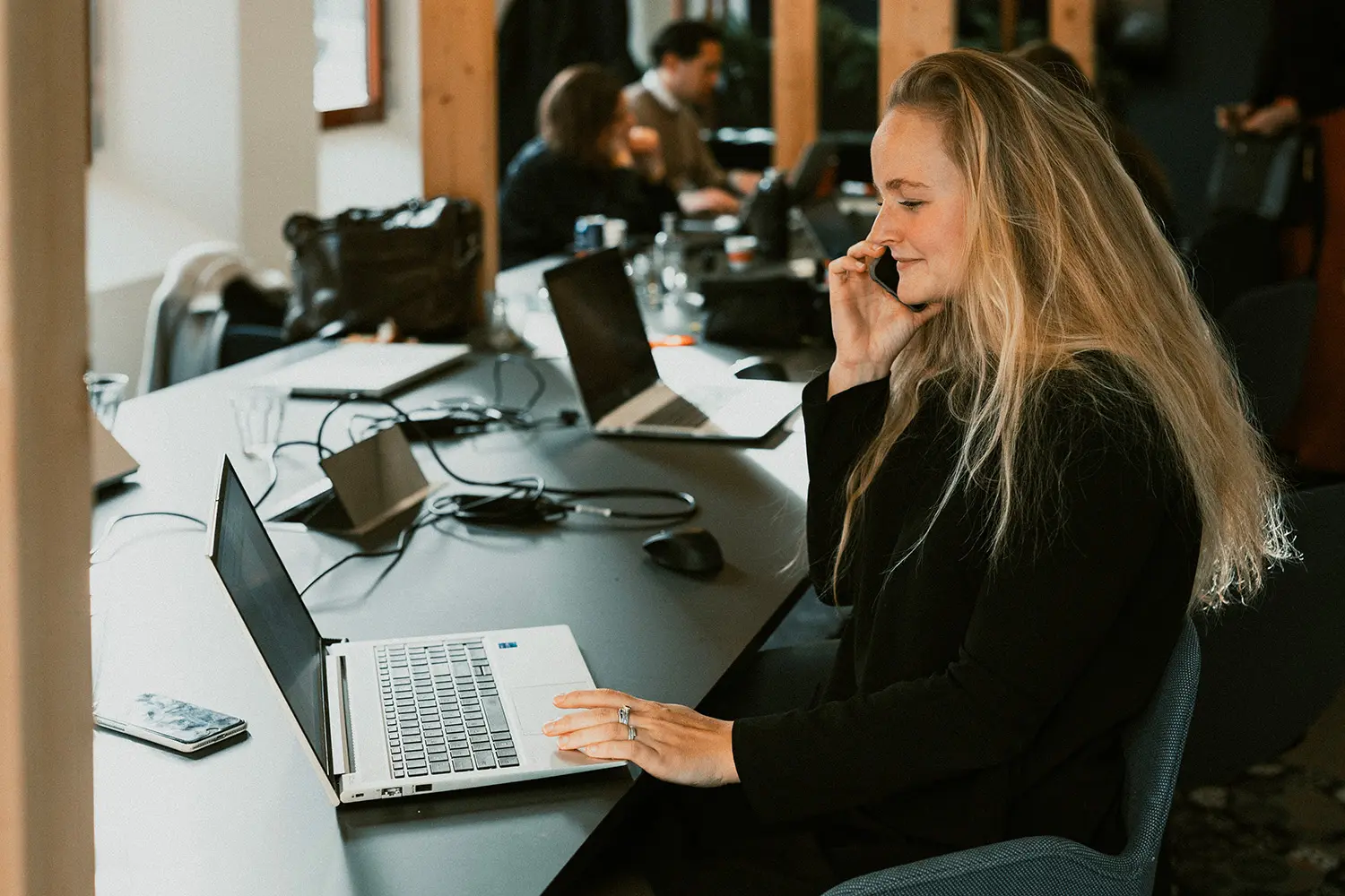 Een vrouw telefoneert en werkt op een laptop in een gedeelde kantoorruimte.