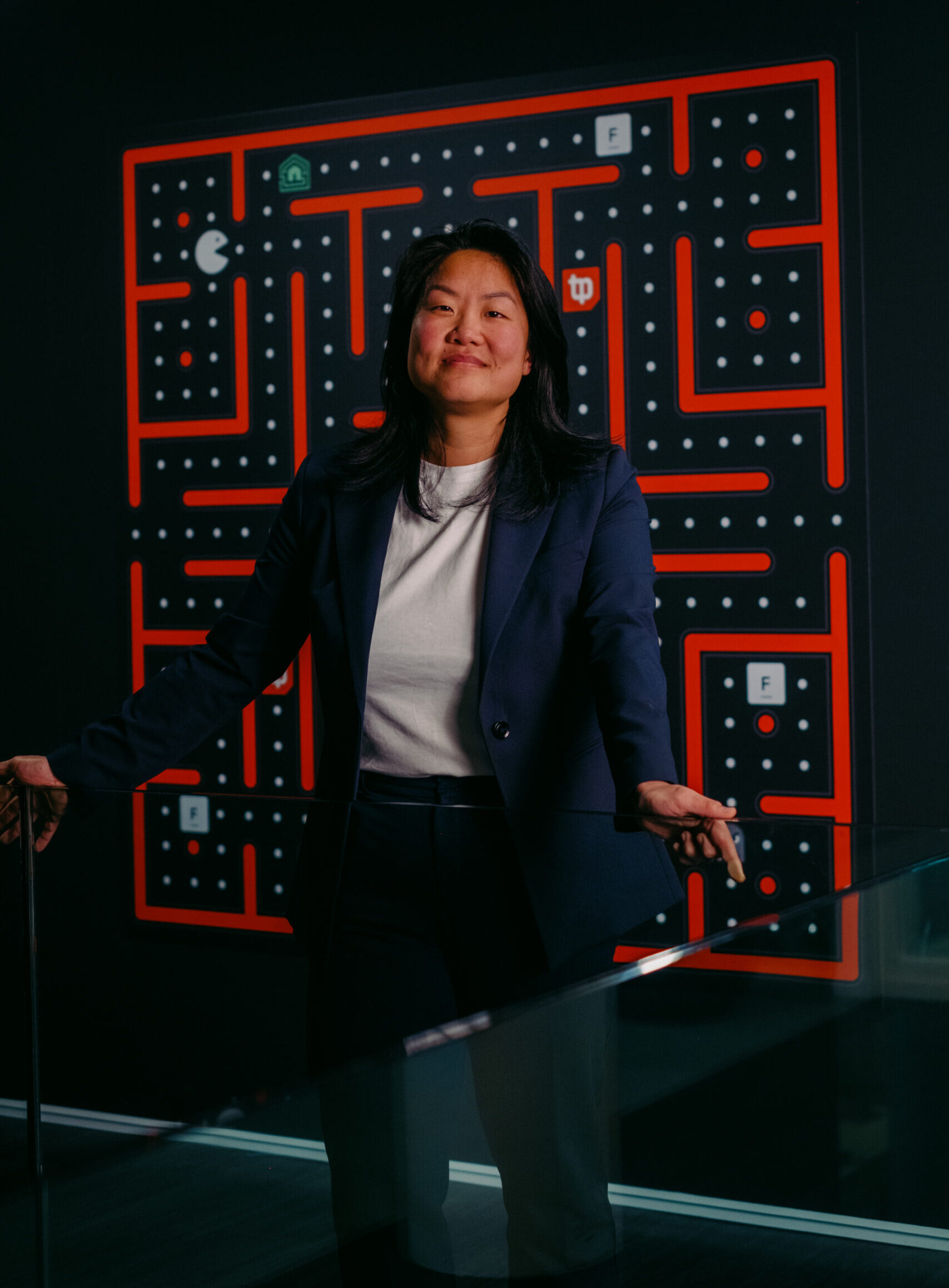 Een vrouw in een blauw pak voor een Pac-Man spelbord op een zwart-wit-rode achtergrond.