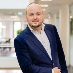 Een man in een donkerblauw pak poseert in een heldere kantooromgeving.