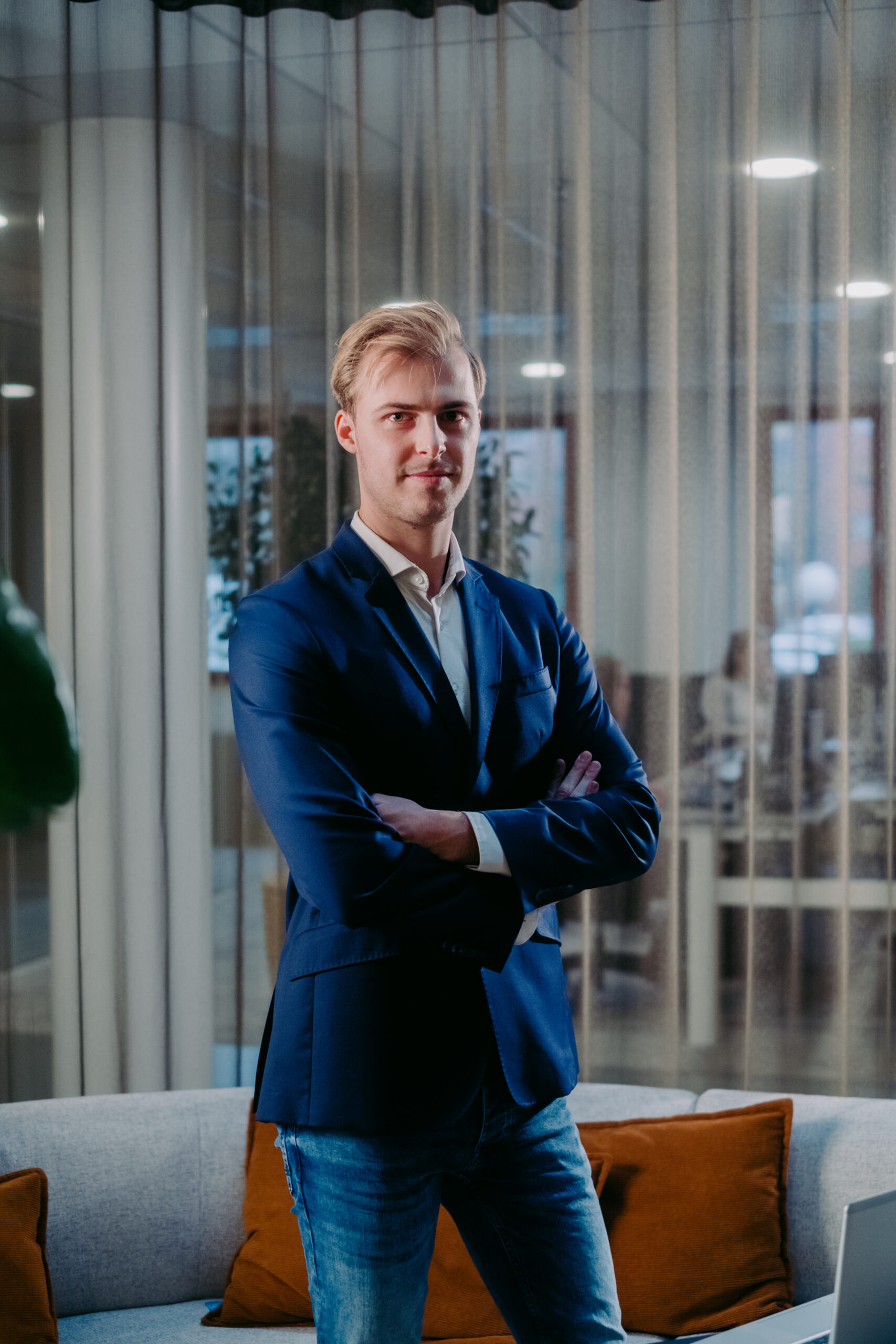 Een man in een blauw pak staat met armen over elkaar in een moderne kantoorruimte.