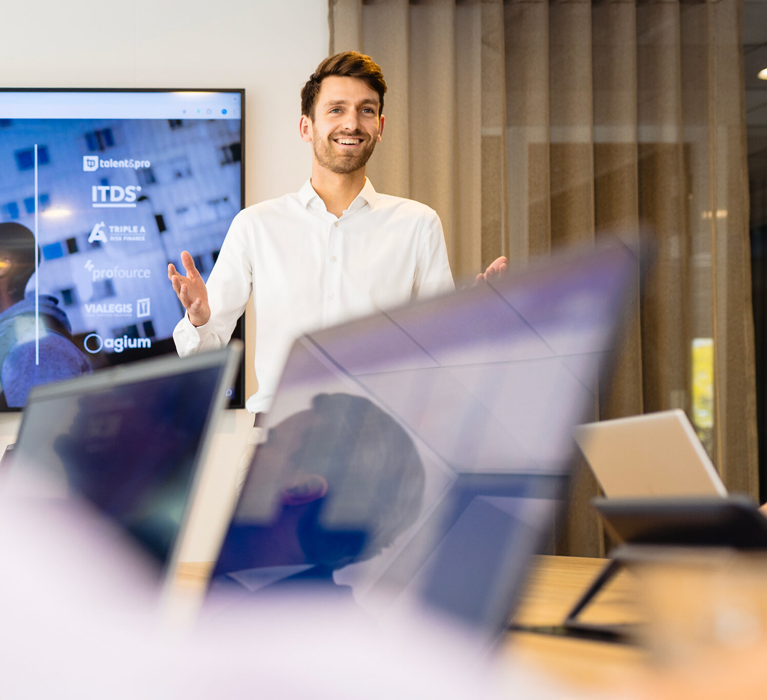 Een man presenteert voor laptops, met een scherm met bedrijfslogo's op de achtergrond.
