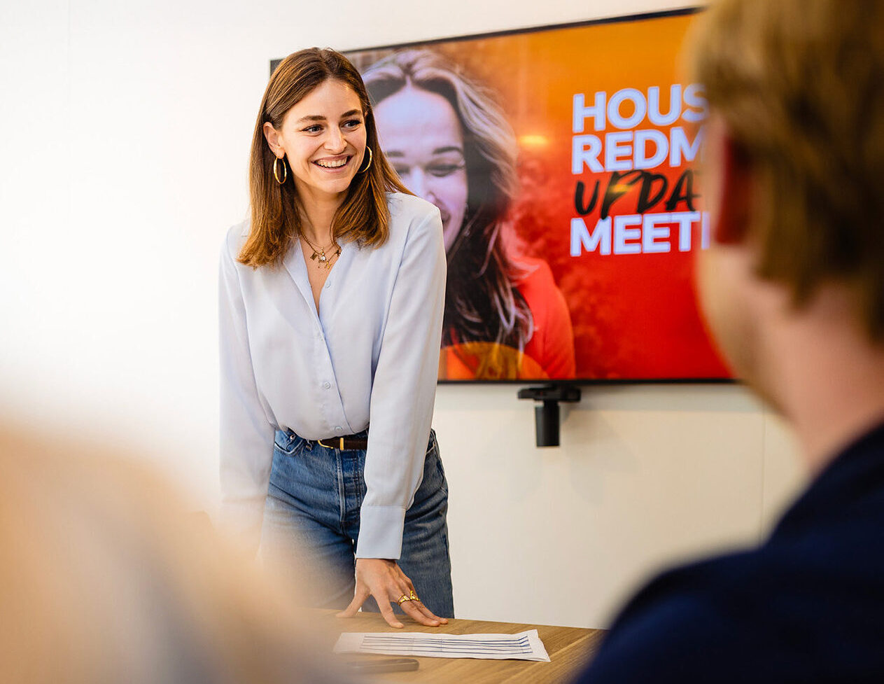 Vrouw glimlacht tijdens presentatie in kantoor met scherm op achtergrond.