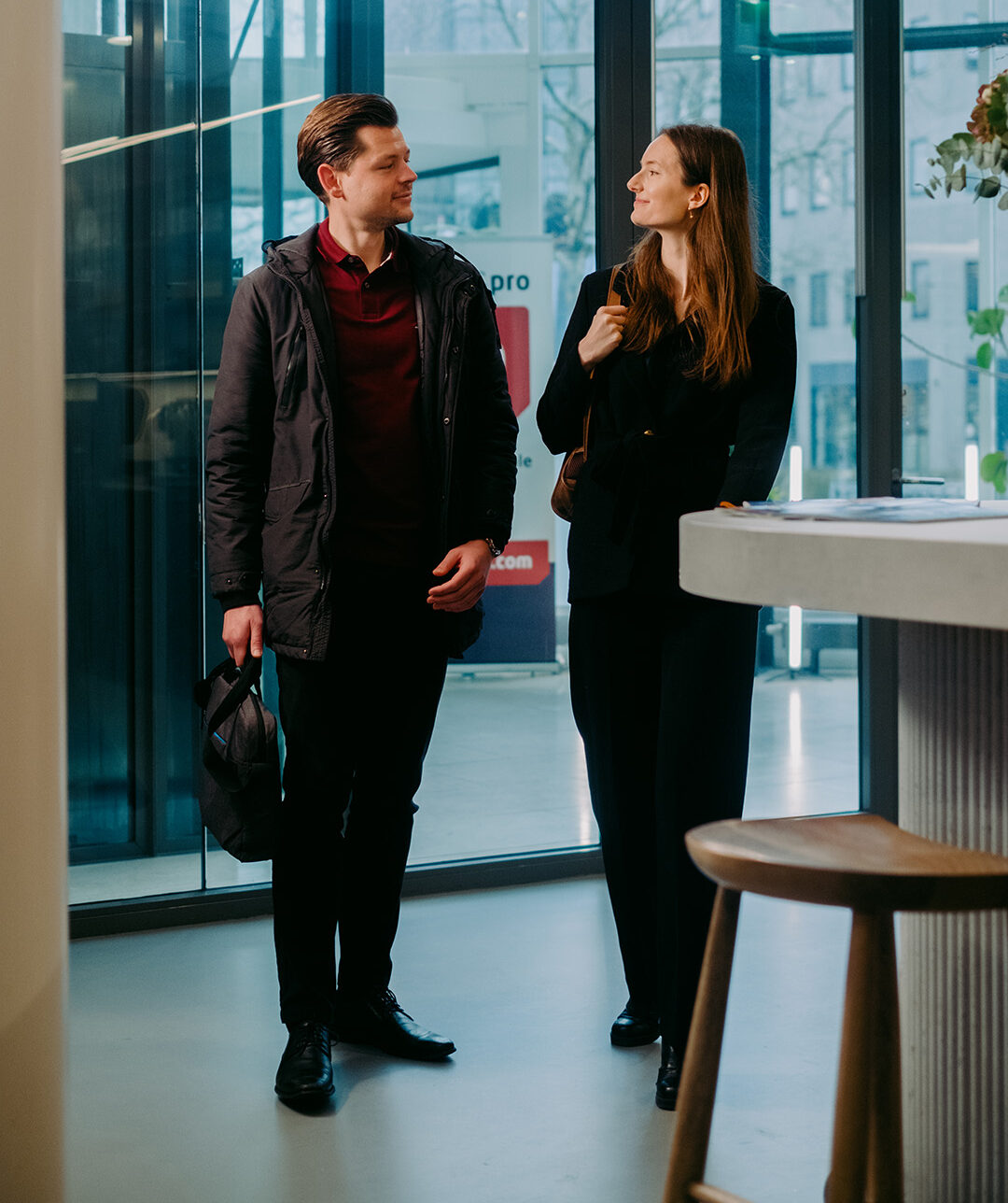 Een man en een vrouw praten glimlachend in een moderne kantoorruimte naast een hoge tafel.